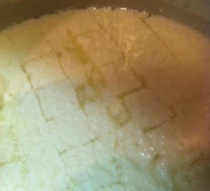 Curds cut now in cubes. Greenish color liquid is whey. White is curd.